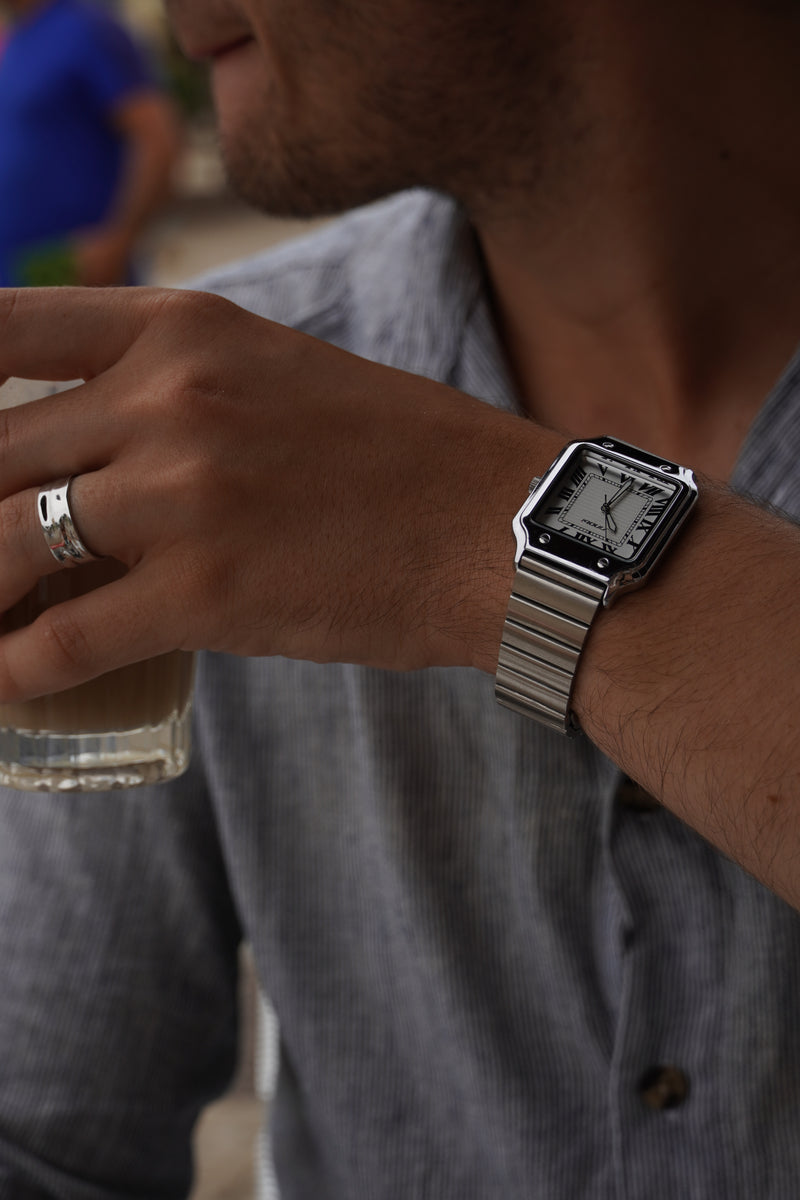 The Moura watch and steel bracelet on the wrist beside a shirt cuff.